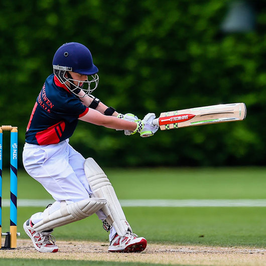 Boy in helmet and pads whacks a cricket ball