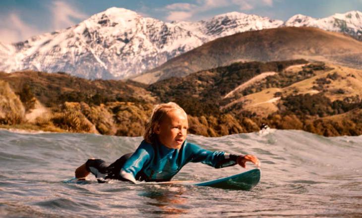 Tamariki paddles surfboard out to the incoming set