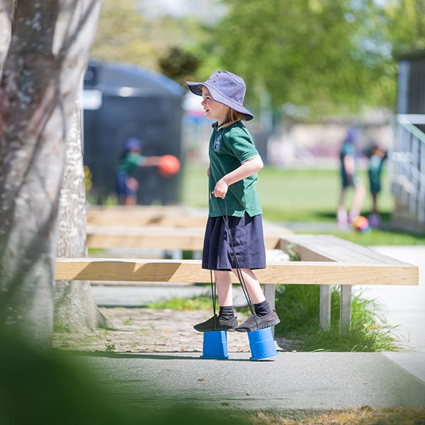 Tamariki/child walking on can stilts
