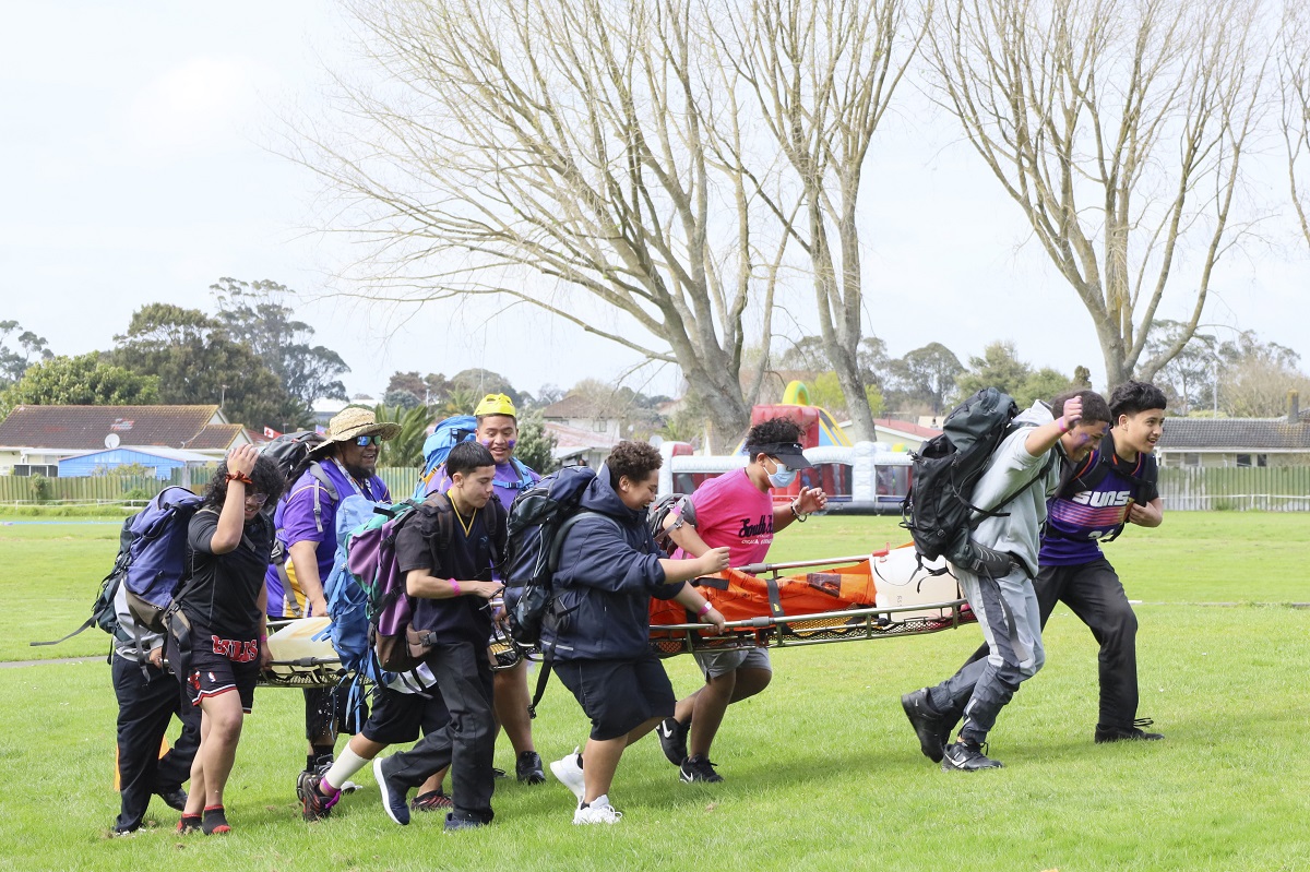 Rangatahi running across a field holding rescue packs