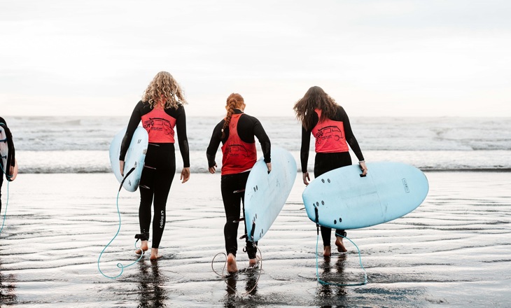 Young women holding surfboard looking out to the waves